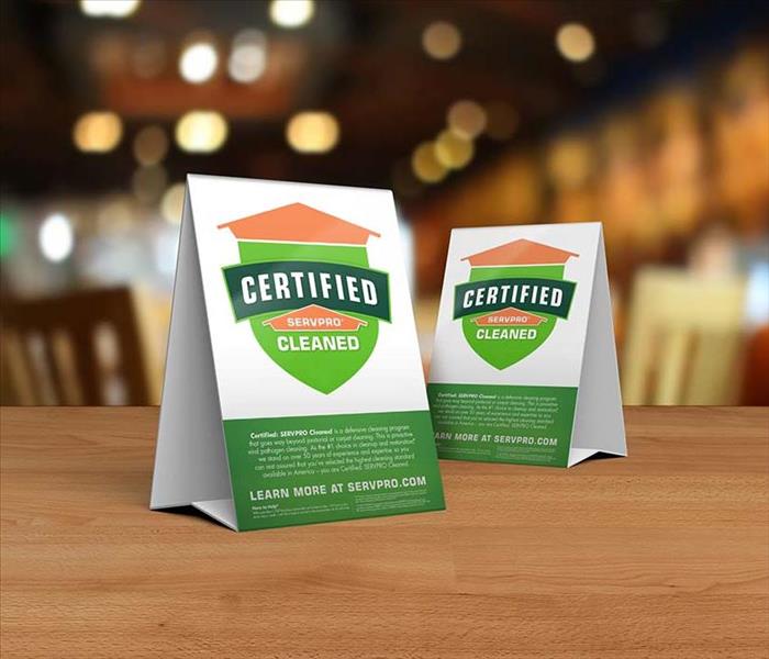 Table tent signs describing the Certified: SERVPRO Cleaned program on top of a wooden table.
